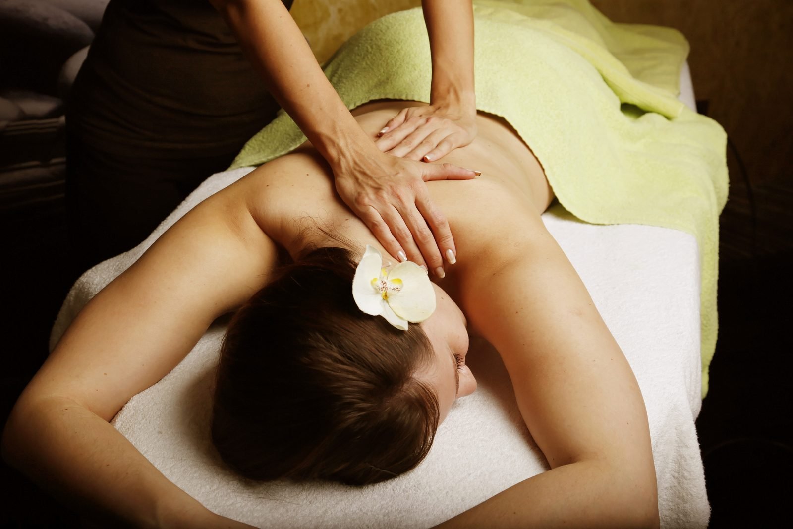 Back massage on a spa table with a white orchid and warm light