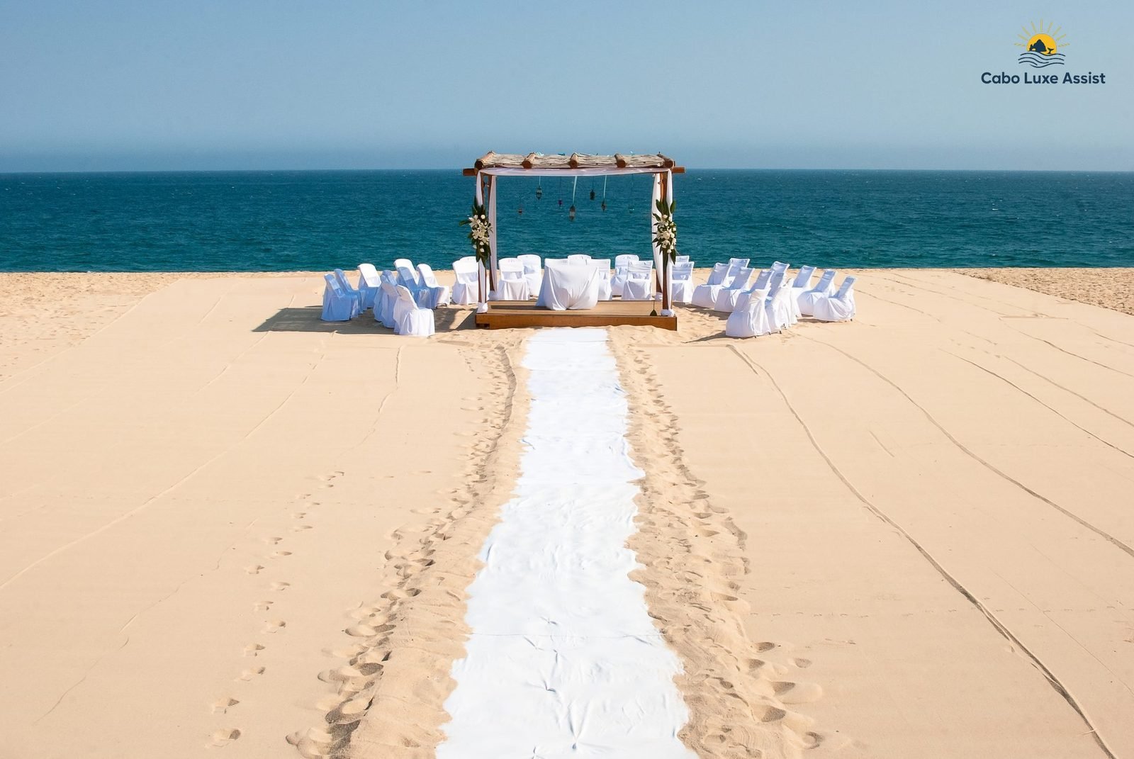 White aisle on the sand leading to a beach wedding pergola, the ocean behind, in Cabo